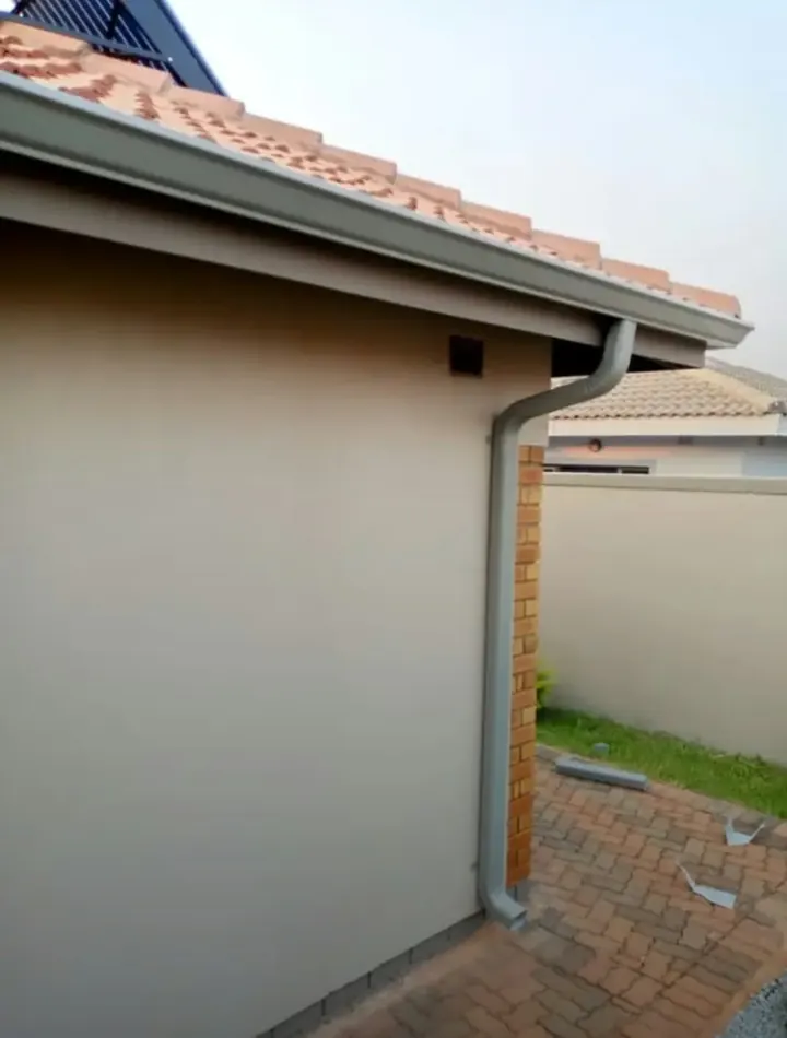 Grey gutter and downpipe under a tiled roof